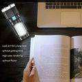 Person reading a book with a flashlight on a desk next to a laptop