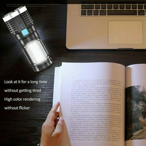 Person reading a book with a flashlight on a desk next to a laptop