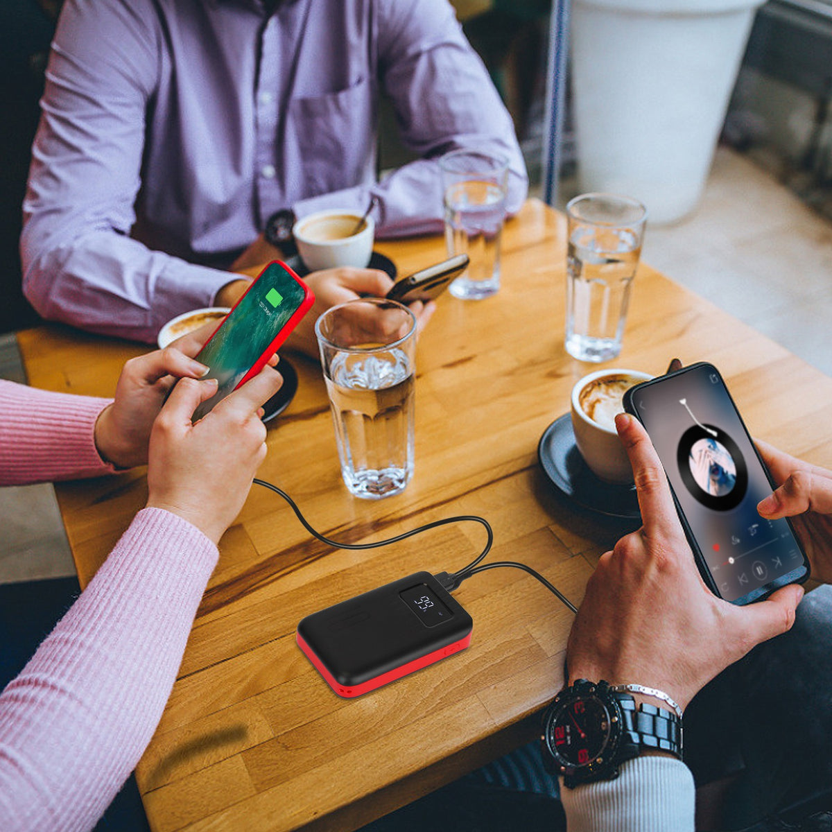 Two people using smartphones at a table with drinks and a power bank.