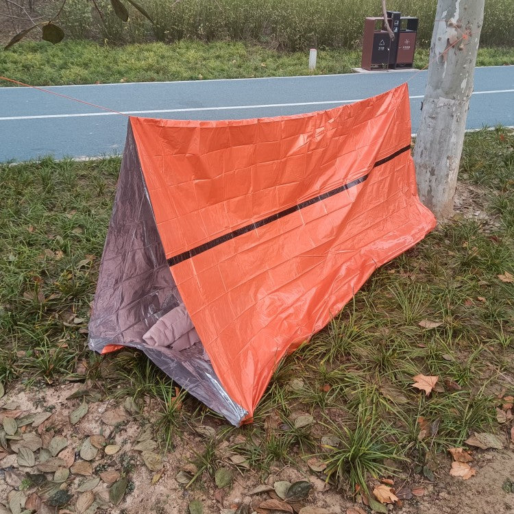 Orange tarp covering a camping setup on a grassy area near a road.