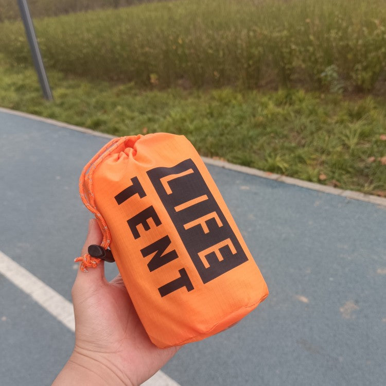 Orange 'LIFE TENT' pouch held in a hand with a grassy field in the background