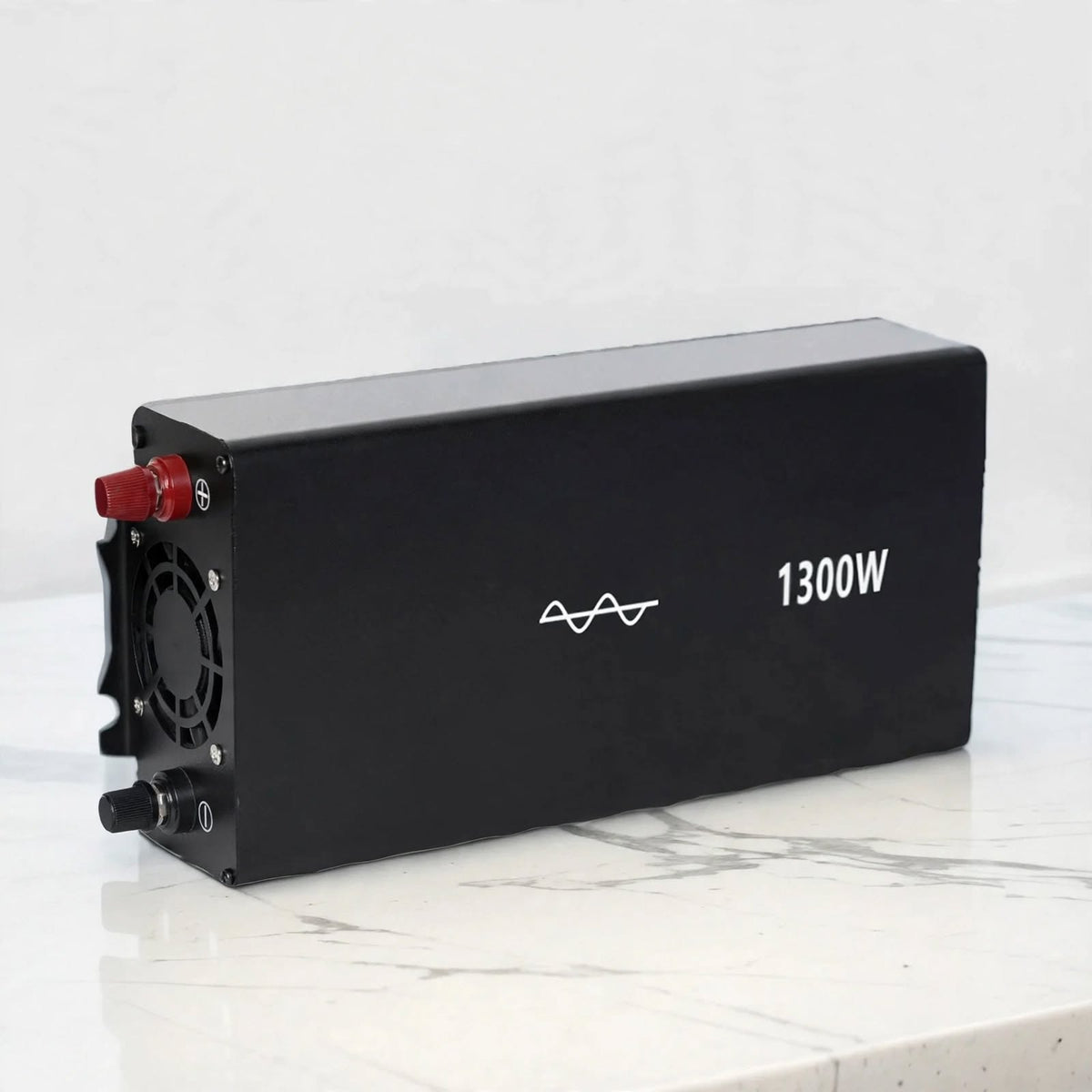 A black rectangular battery or power unit with a cooling fan on one end, a red terminal cap, and white printed text reading 1300W, photographed on a light marble-like surface against a pale background.