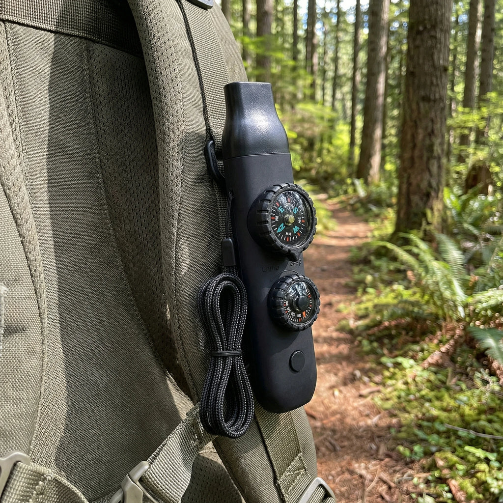 Black compass and lanyard attached to a green backpack in a forest setting