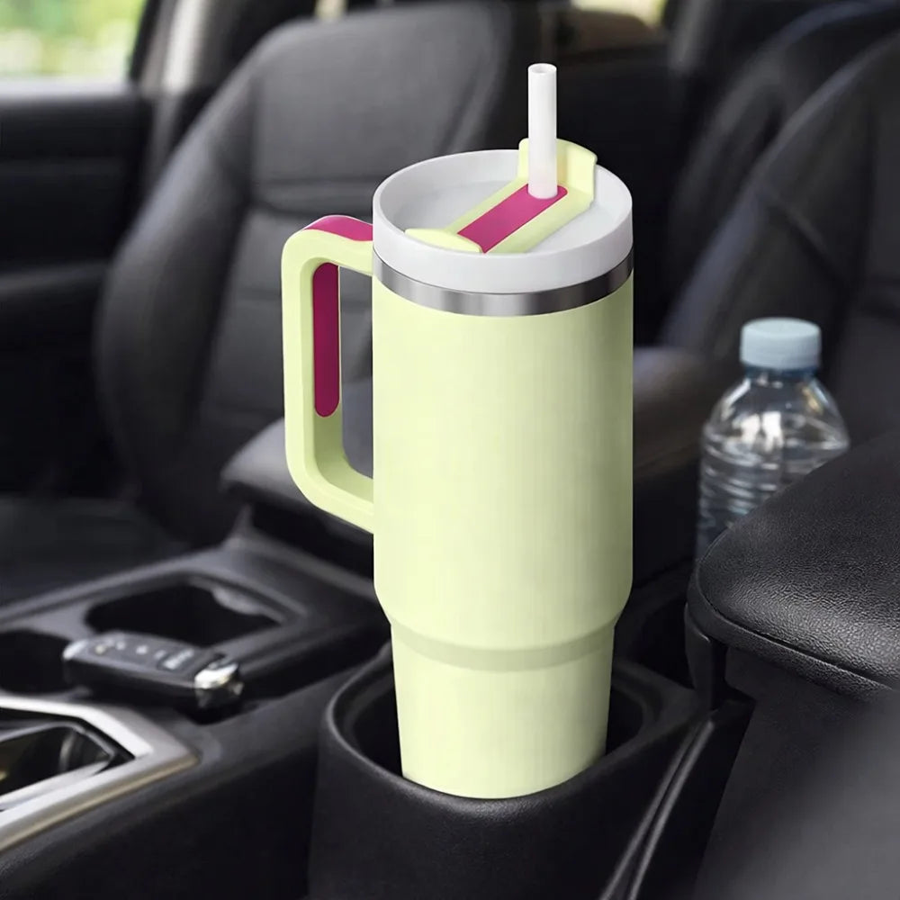 Green mug with handle and straw in a car cup holder, next to a water bottle.