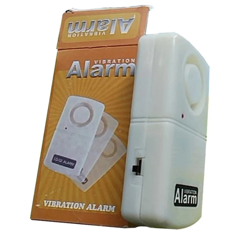 A white plastic vibration alarm device standing next to its orange and white retail box, with the product name 'Vibration Alarm' visible on both the packaging and the device.