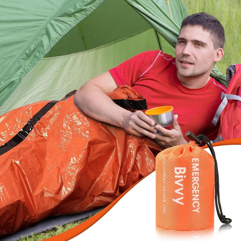 Man sitting inside an orange emergency bivvy with a green tent in the background