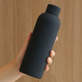 Hand holding a black water bottle against a wooden background