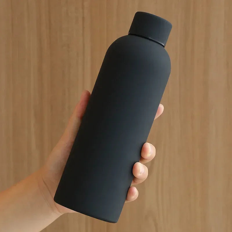 Hand holding a black water bottle against a wooden background